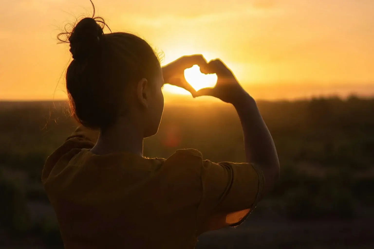 Woman with hands in a heart shape over sunrise