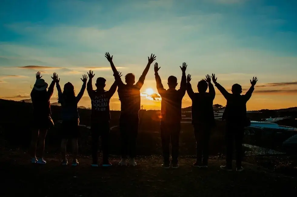 Group of people with hands up looking at sunrise